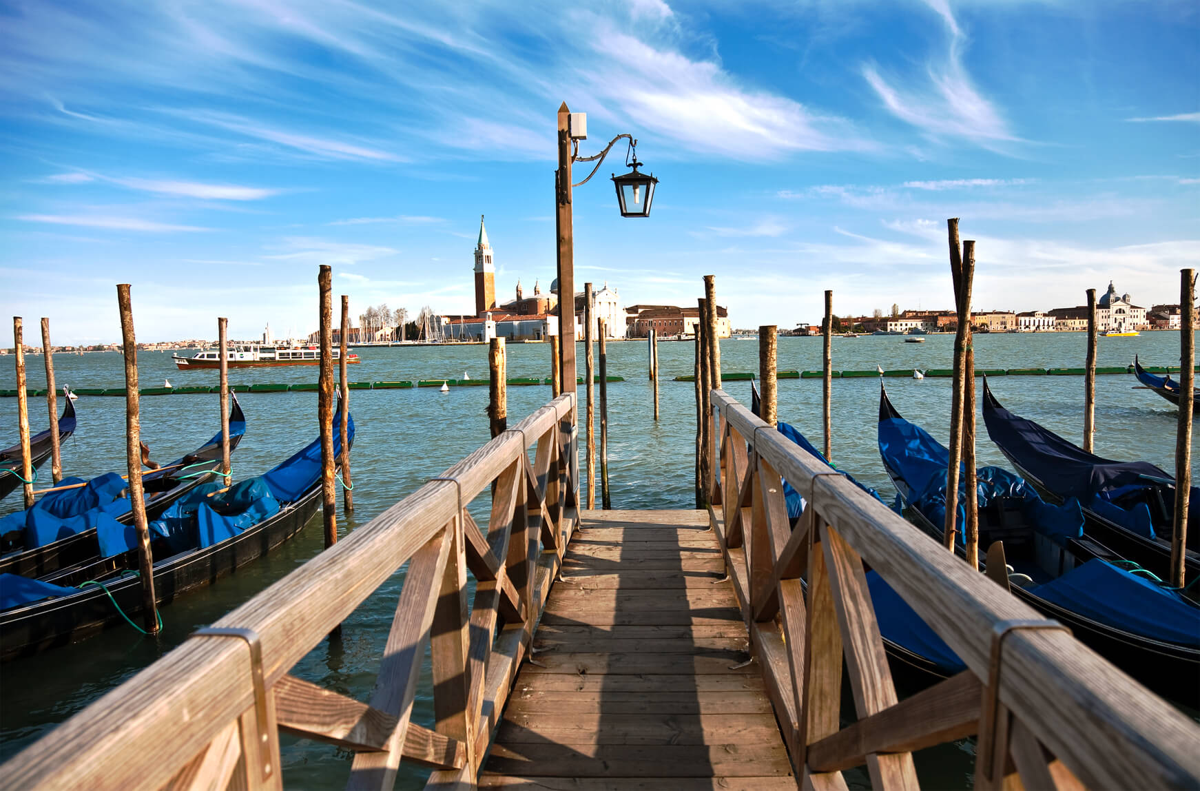 Wooden dock with gondolas and a church in the distance.