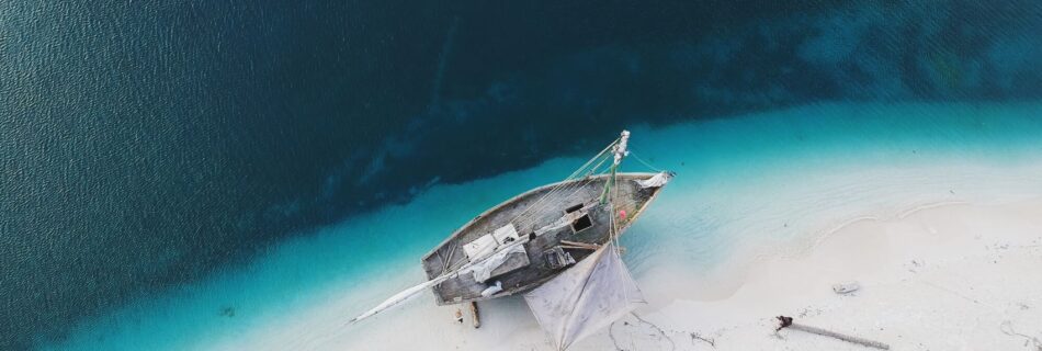 Boat on a sandy beach by turquoise water.