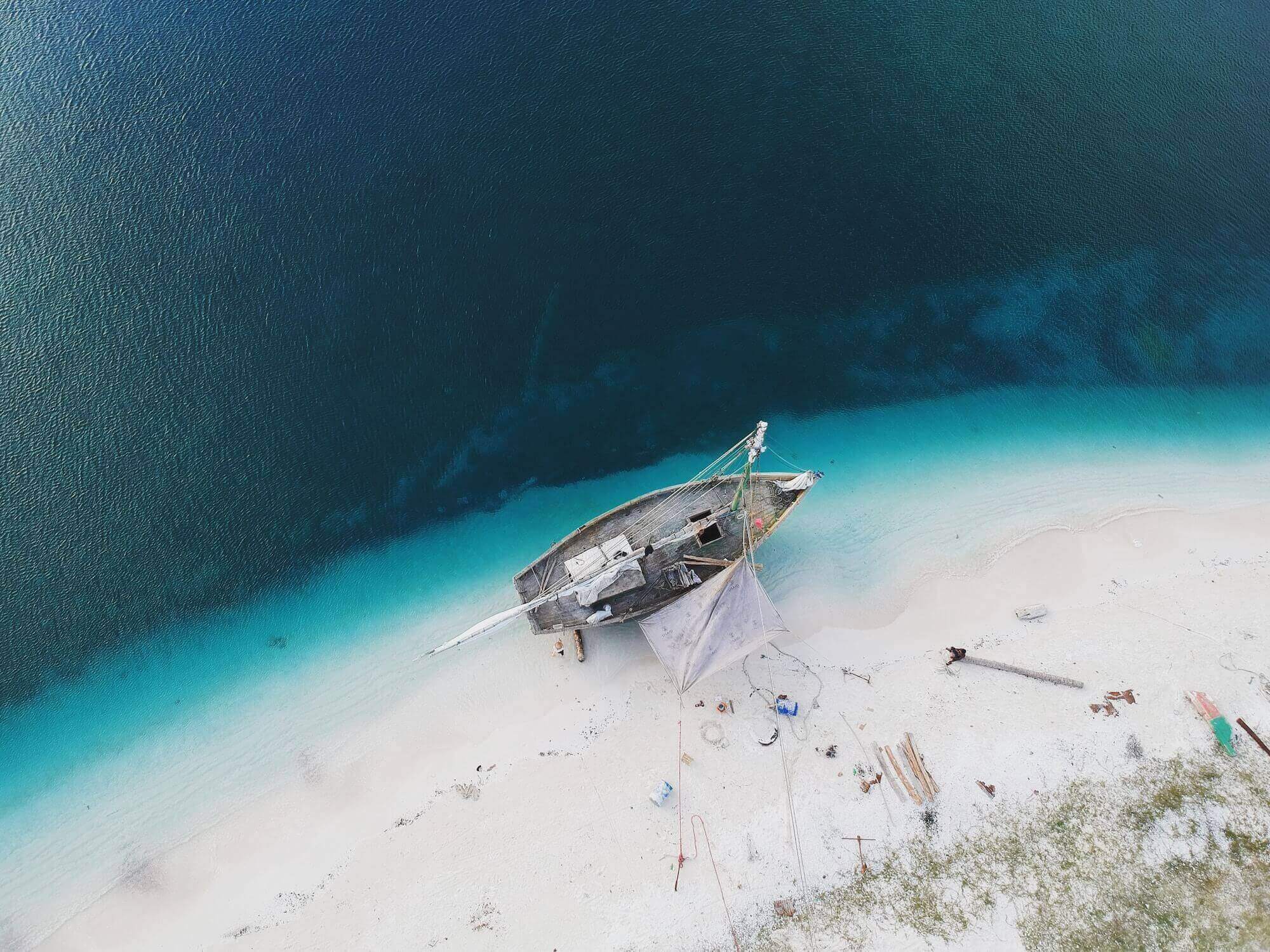 Boat on a sandy beach by turquoise water.