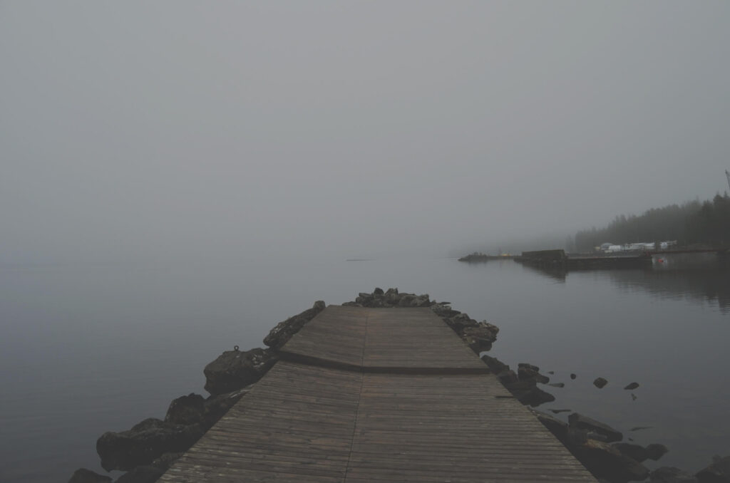 Foggy wooden dock extending into lake.